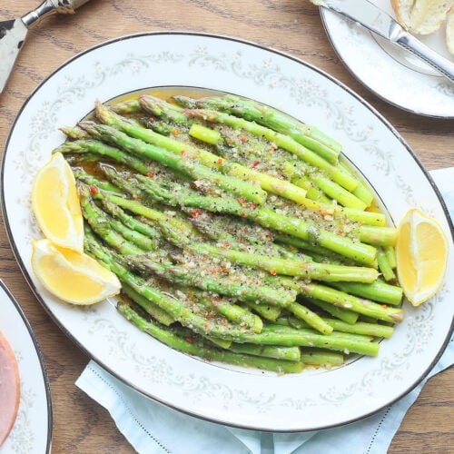 marinated asparagus in a white decorative serving dish with lemon wedges on the side