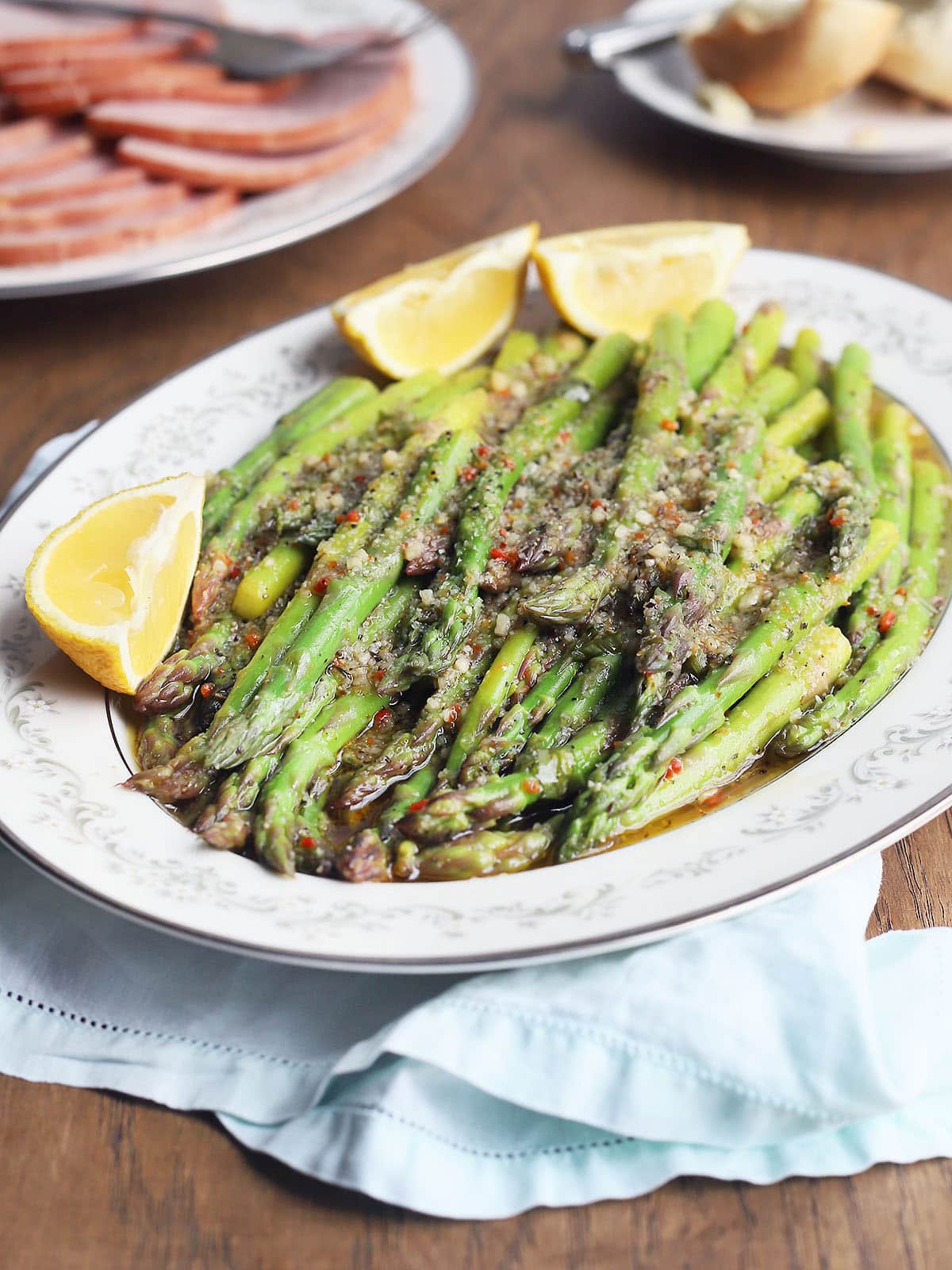 marinated asparagus in a white decorative serving dish with lemon wedges on the side