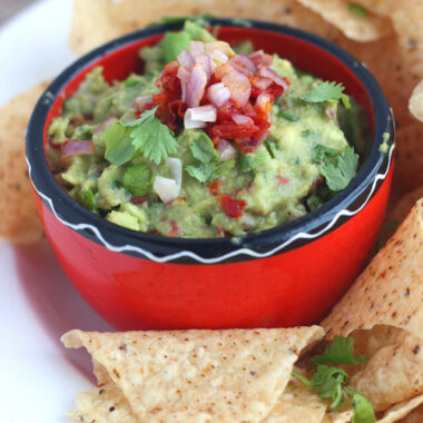 homemade guacamole in a red and black bowl with chips on the side