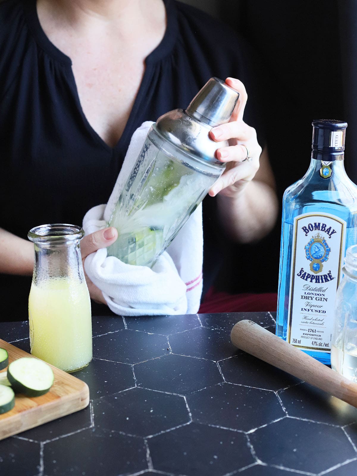 person shaking a cocktail shaker with cucumber gimlet ingredients inside.