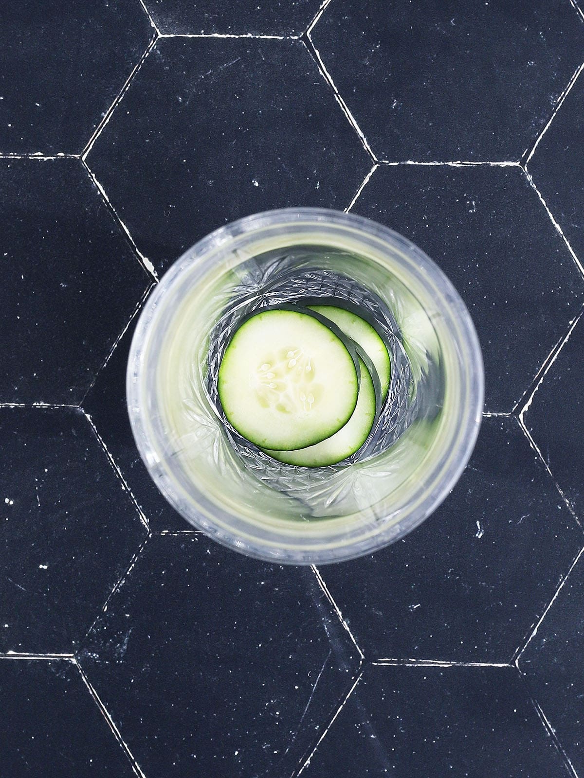 four cucumber slices in the bottom of a glass cocktail shaker.