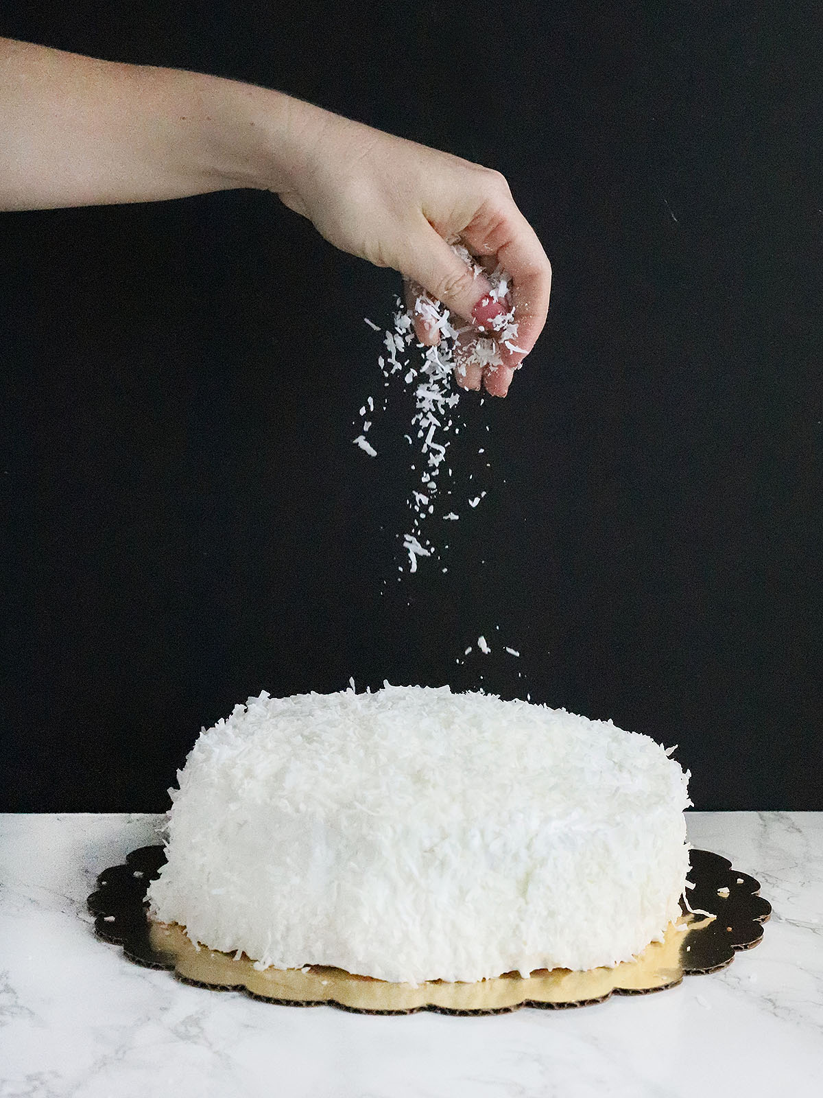 hand sprinkling coconut over the top of the coconut cake