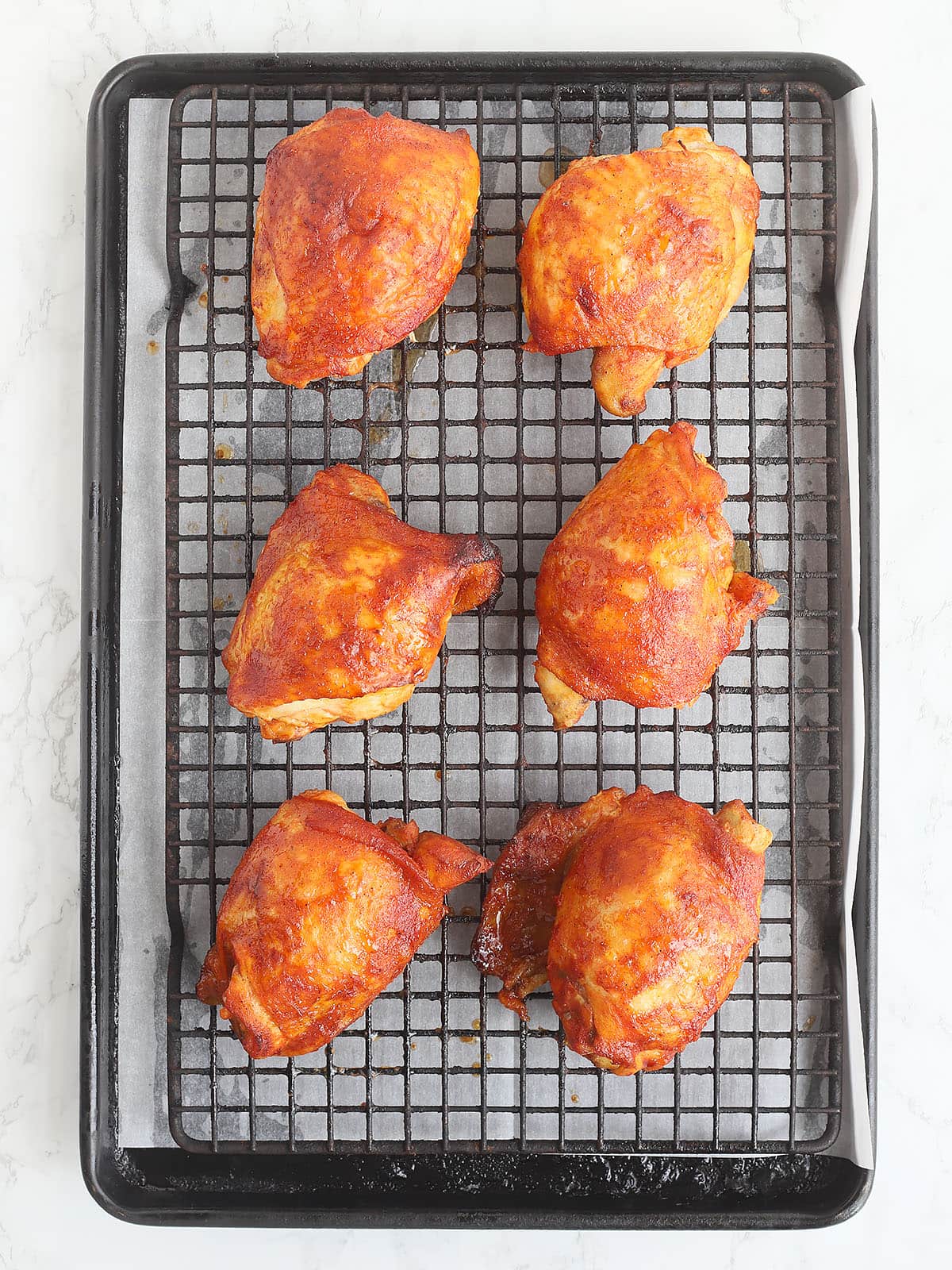 six pieces of oven baked BBQ chicken thighs on a baking rack after coming out of the oven.