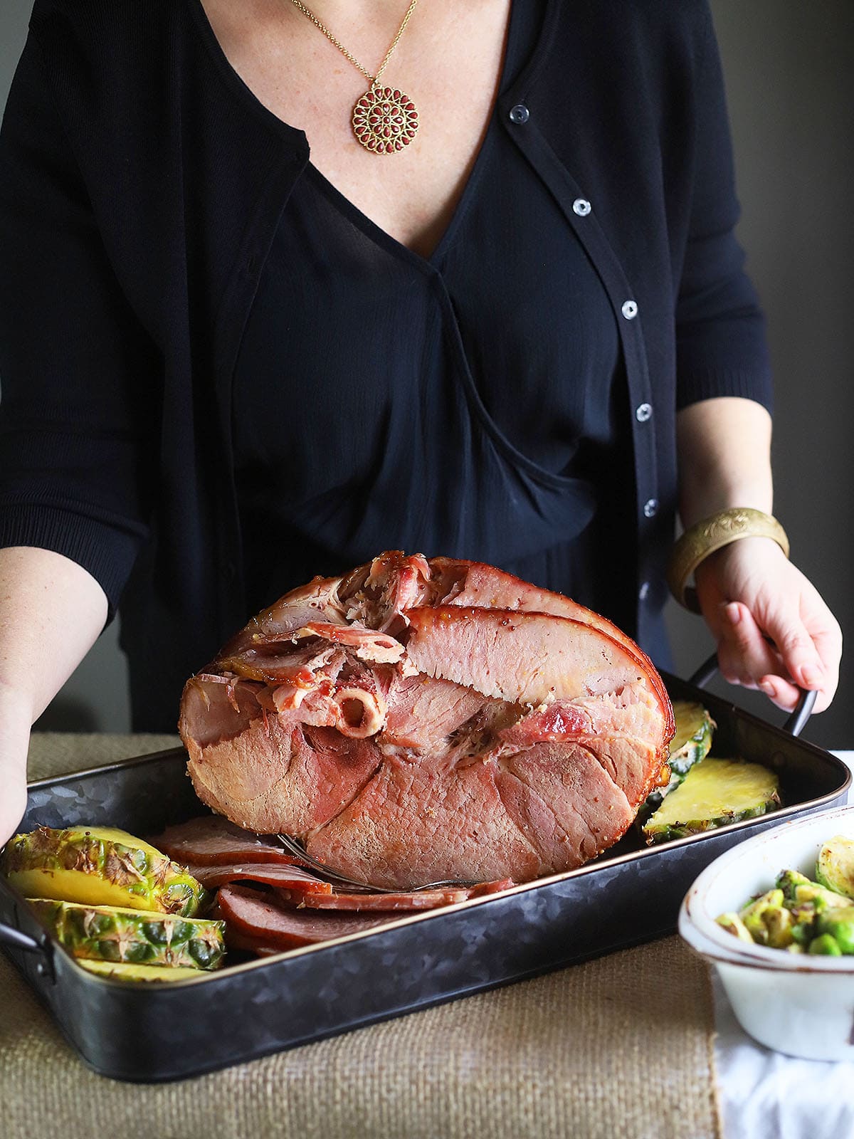 woman placing a metal serving pan with pineapple glazed ham and pineapple slices on a table