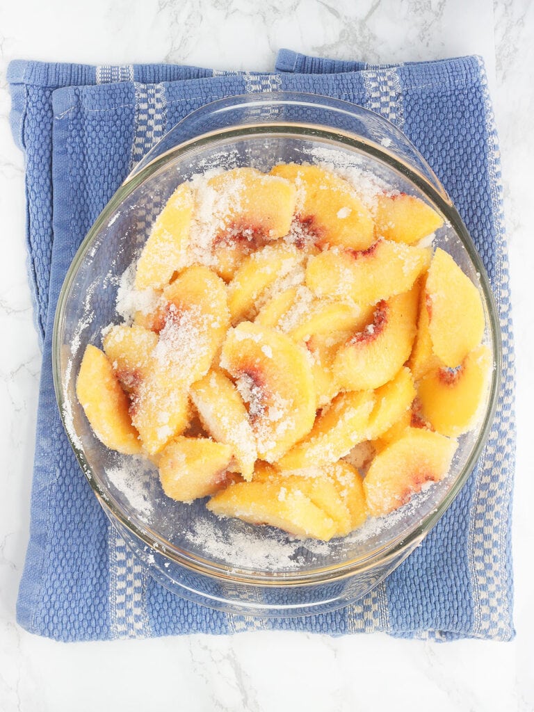 sliced peaches mixed with sugar in a glass mixing bowl