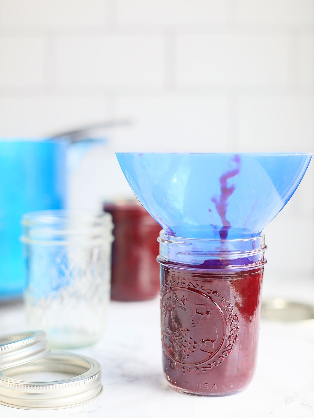 filling a jar of blackberry jam with a blue funnel