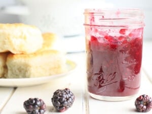 a jar of blackberry jam with a plate of biscuits in the background