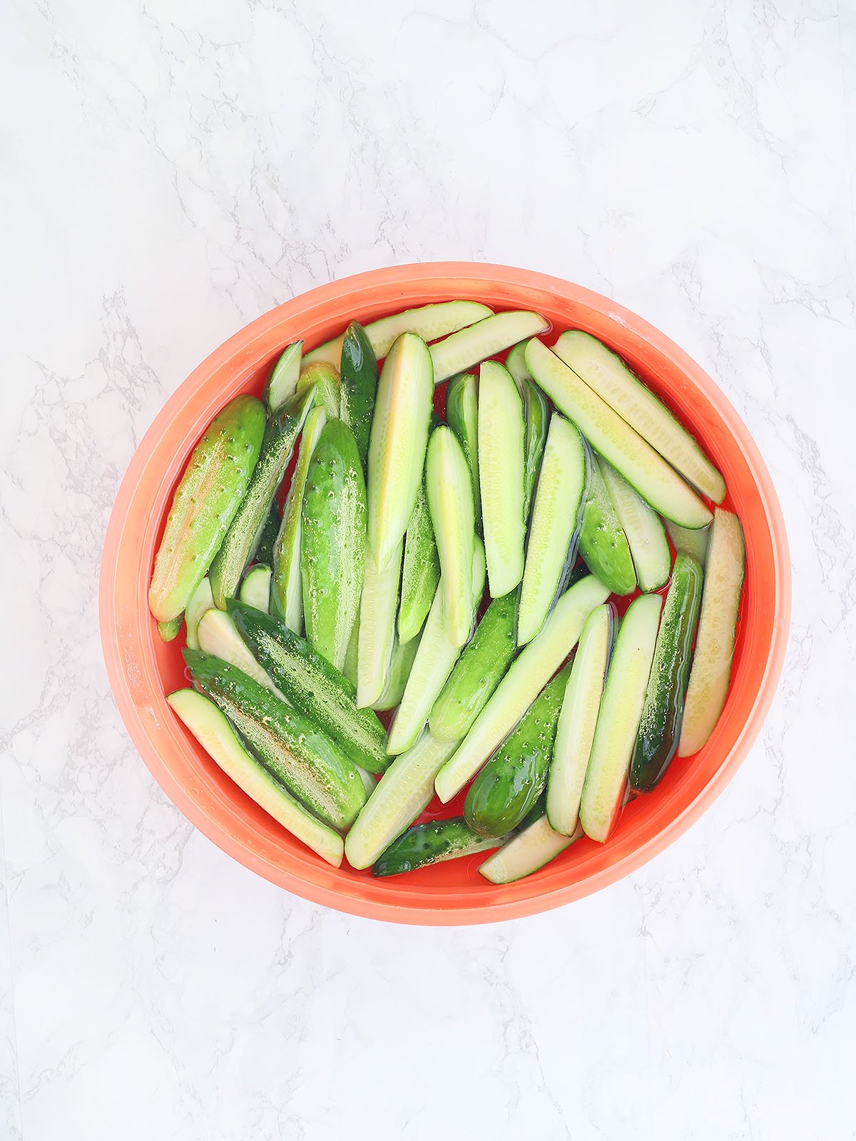 sliced cucumber spears soaking in a large bowl of salt water