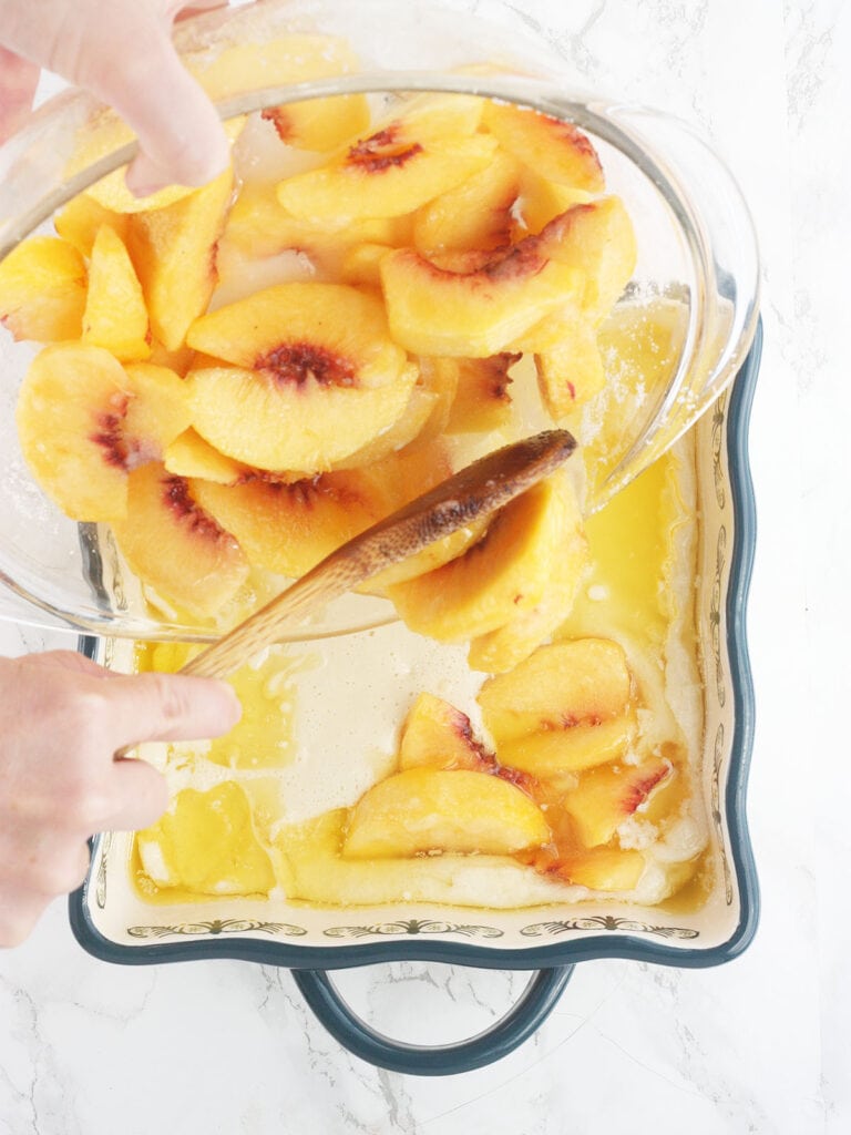 spooning the sliced peaches over the batter and melted butter in a baking dish