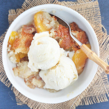 white bowl of peach cobbler topped with a scoop of vanilla ice cream