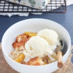 white bowl of peach cobbler topped with a scoop of vanilla ice cream