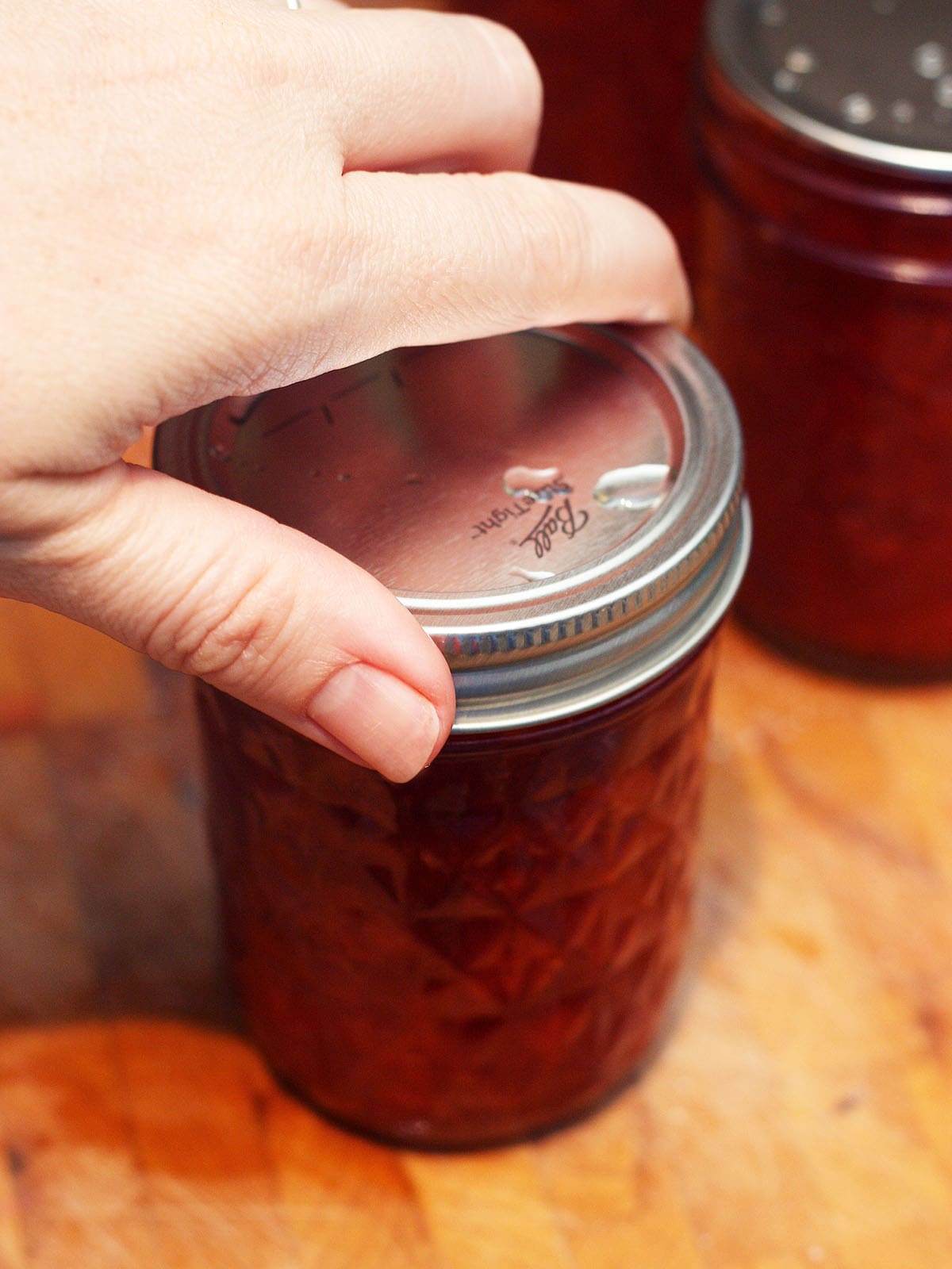 Hand securing rings on a jar of jam that is about the be canned
