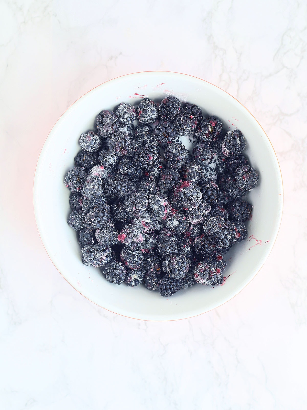 fresh blackberries mixed with sugar in a white mixing bowl