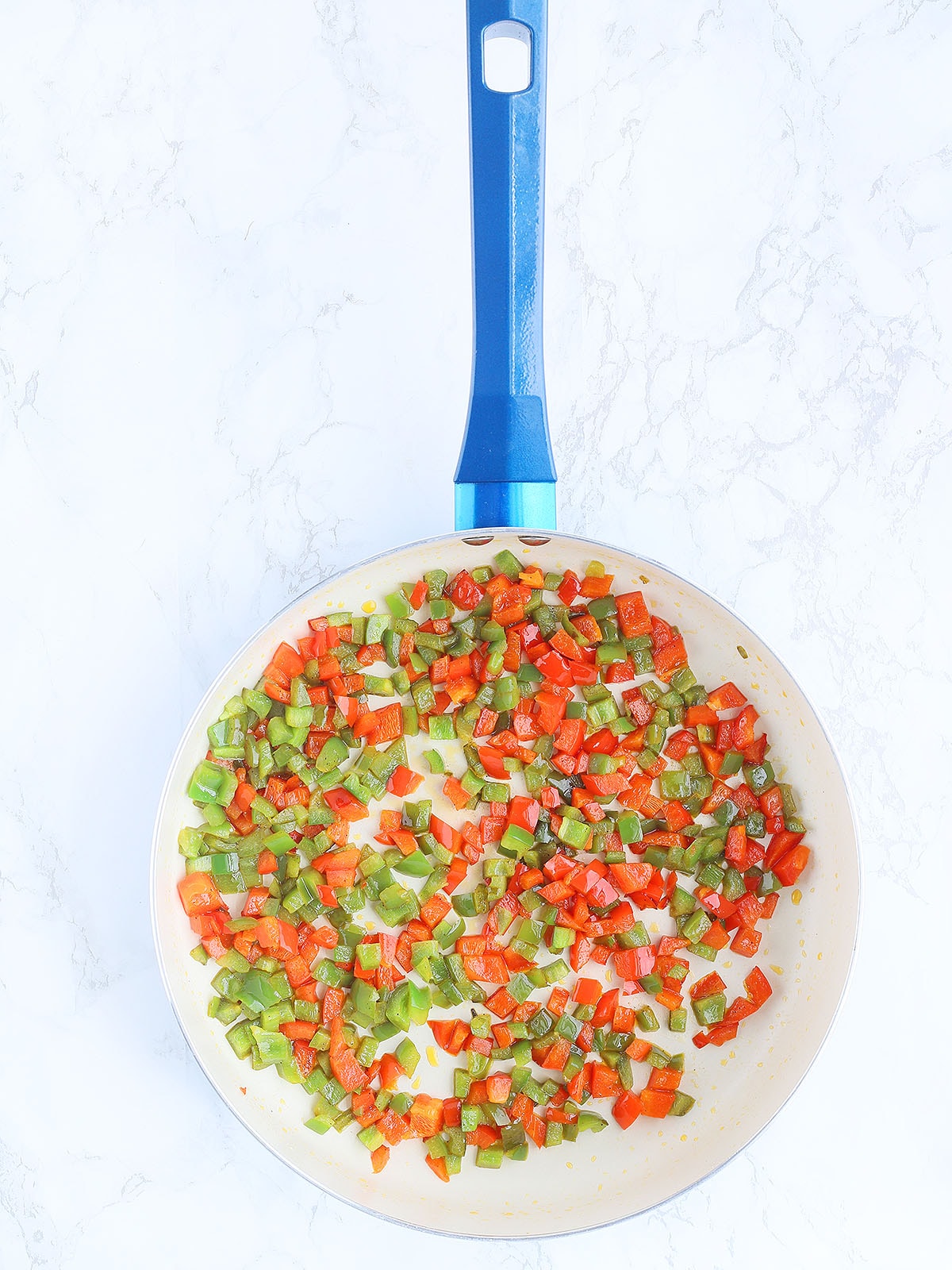 sauteed red and green diced bell peppers in a large blue skillet