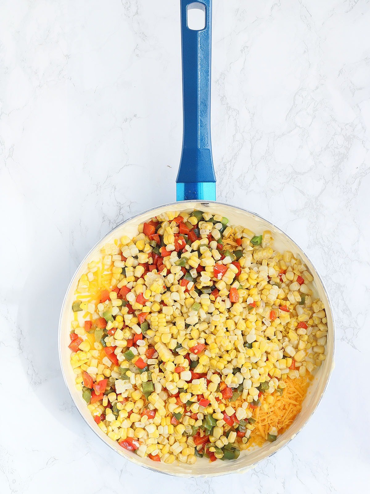 corn, bell pepper, and cheese unmixed in a large blue skillet