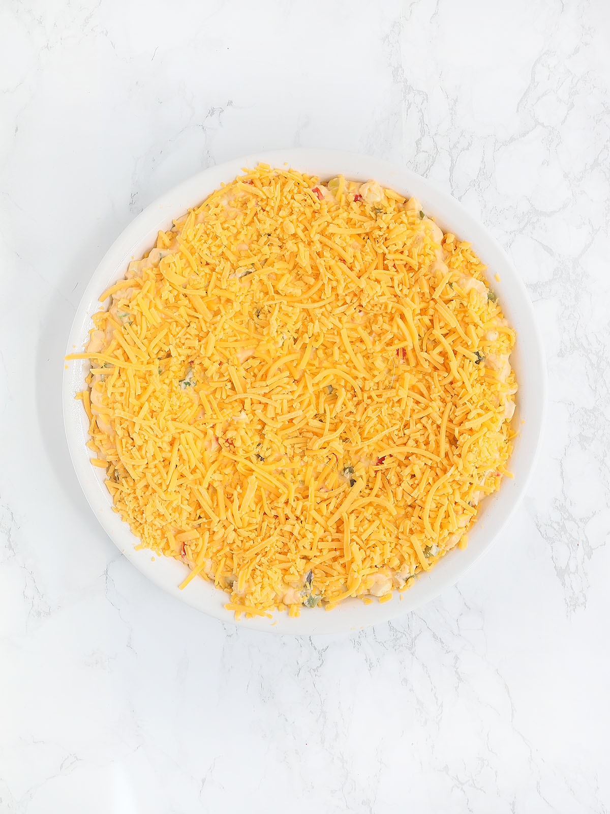 corn dip topped with shredded cheese before it has been baked in the oven