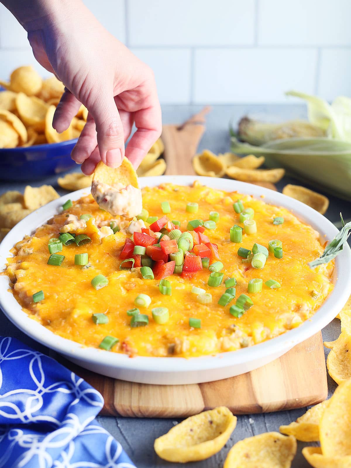 hand dipping a corn chip into a dish of hot corn dip with cream cheese