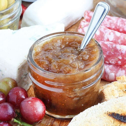 Small jar of fig preserves on a meat and cheese tray.