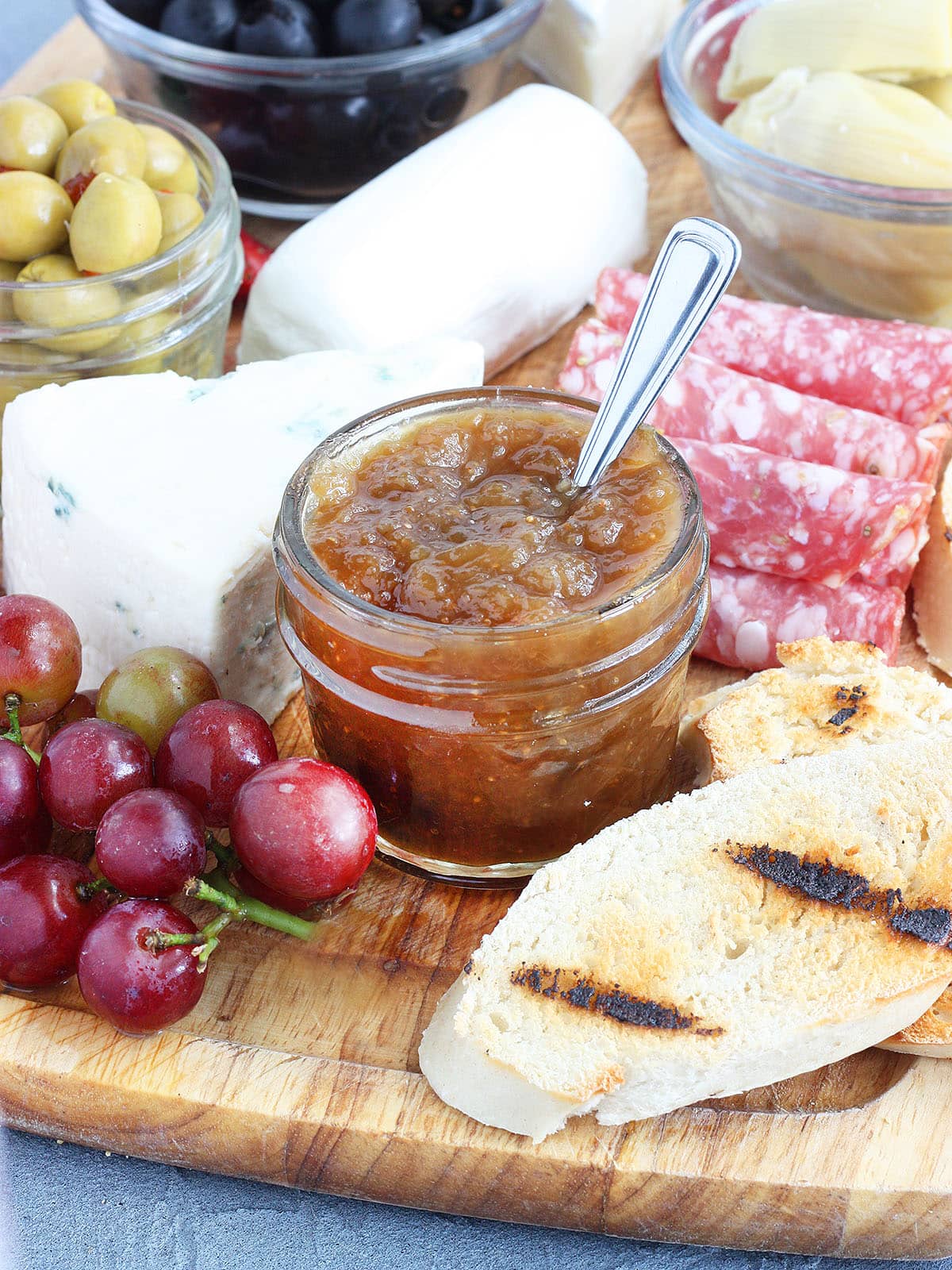 Small jar of fig preserves on a meat and cheese tray.