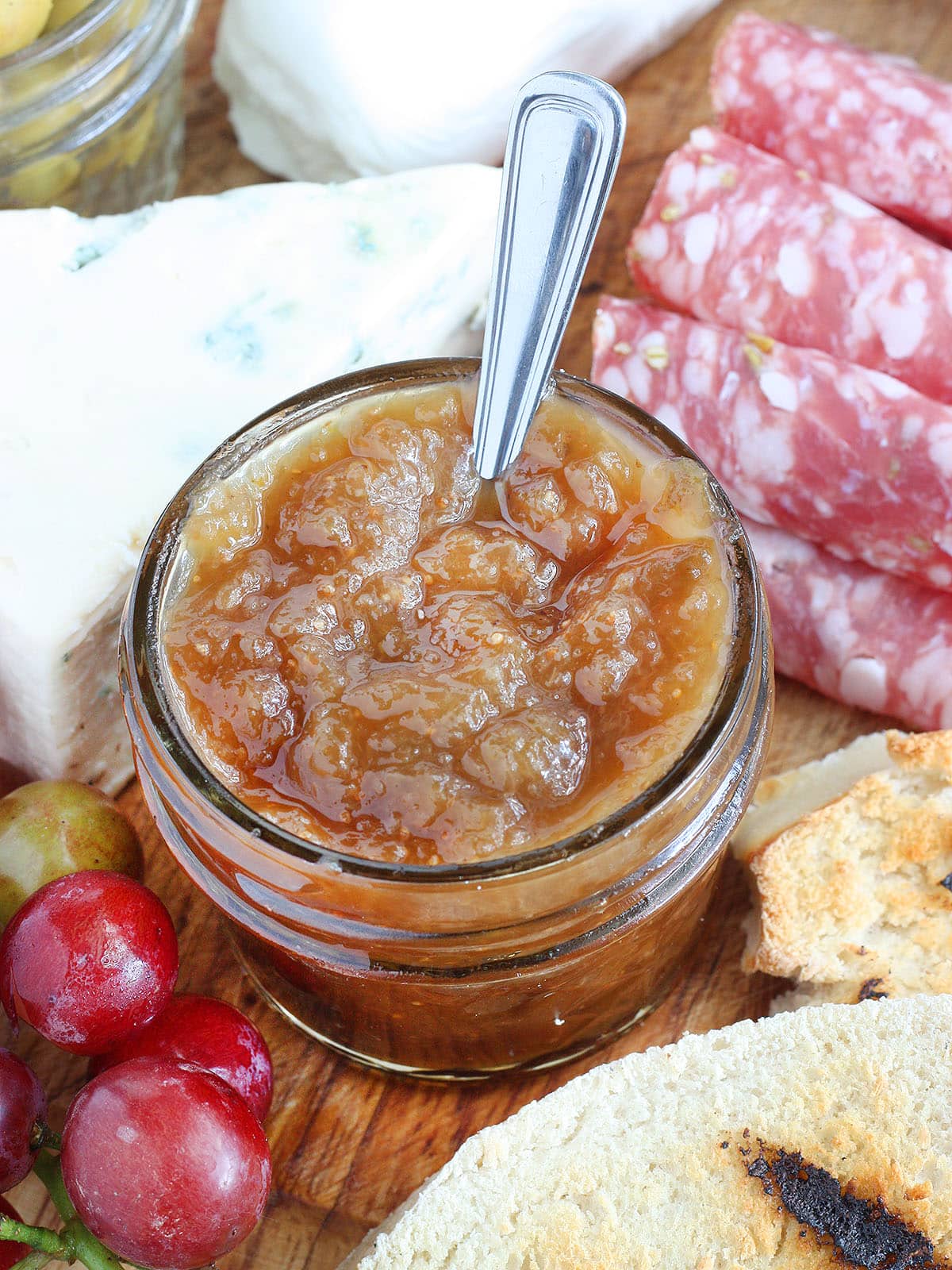 Small jar of fig preserves on a meat and cheese tray.