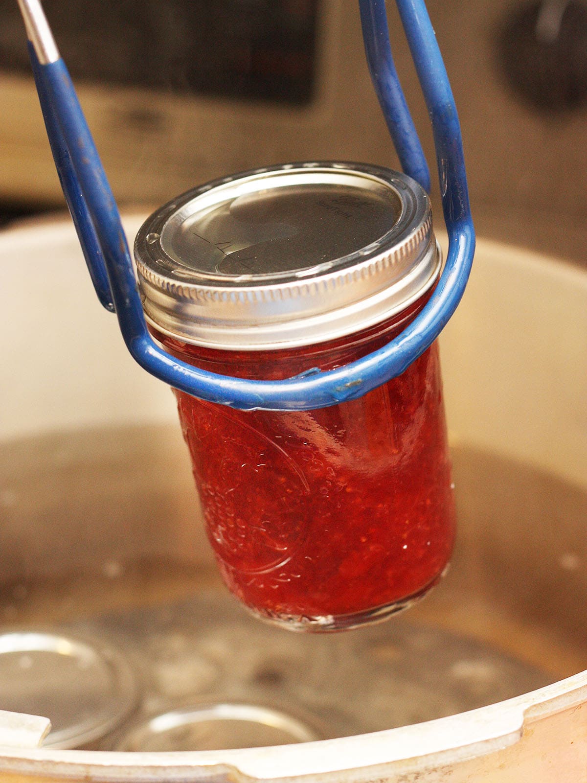 using a jar lifter to remove a jar of jam from a stock pot after water bath canning