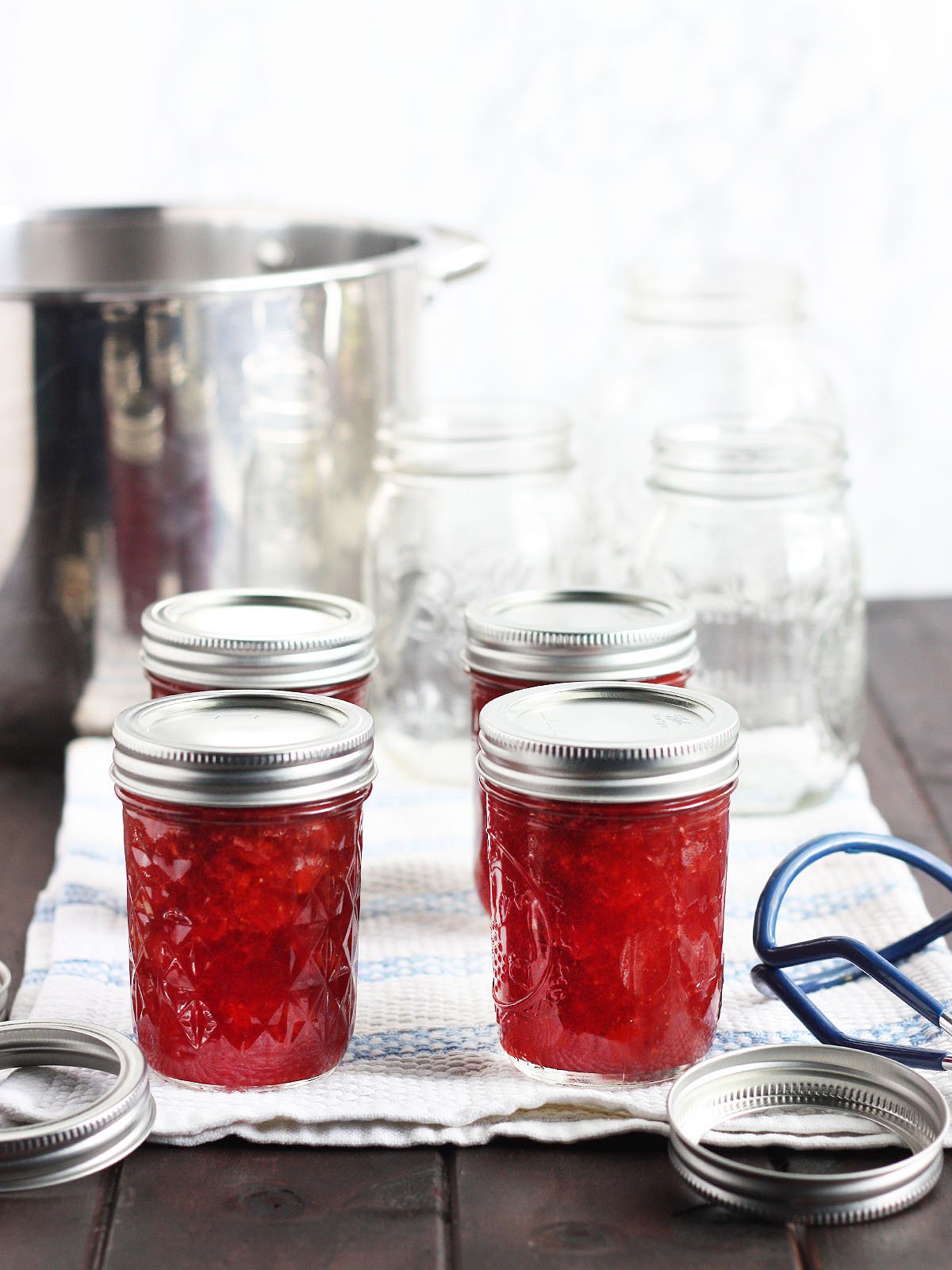 four jars of homemade jam cooling on a towel with empty mason jars and canning rings in the background