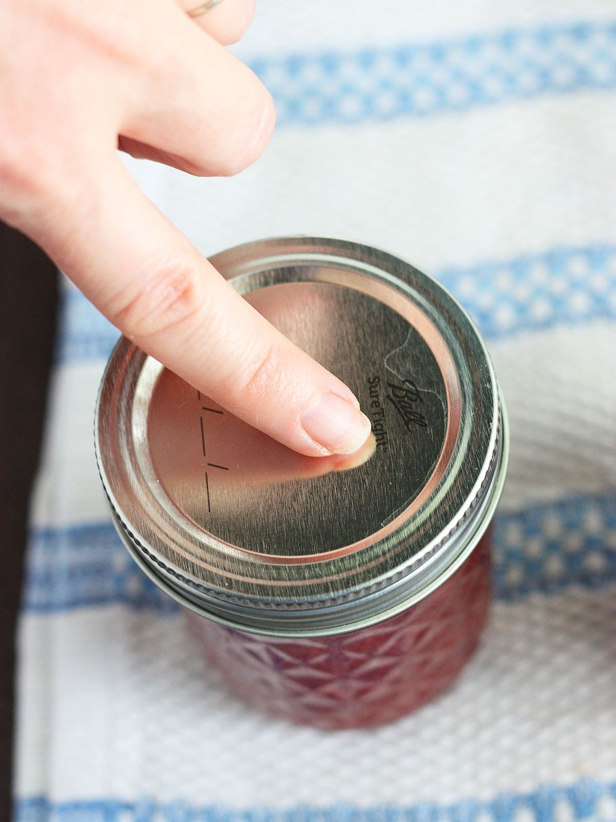 finger pressing down on the center of a lid to check for a seal