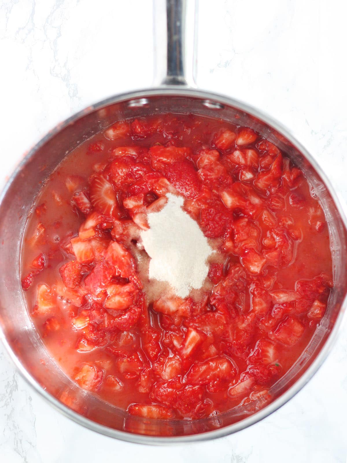Mashed strawberries with lemon juice and pectin in a stainless steel saucepan.