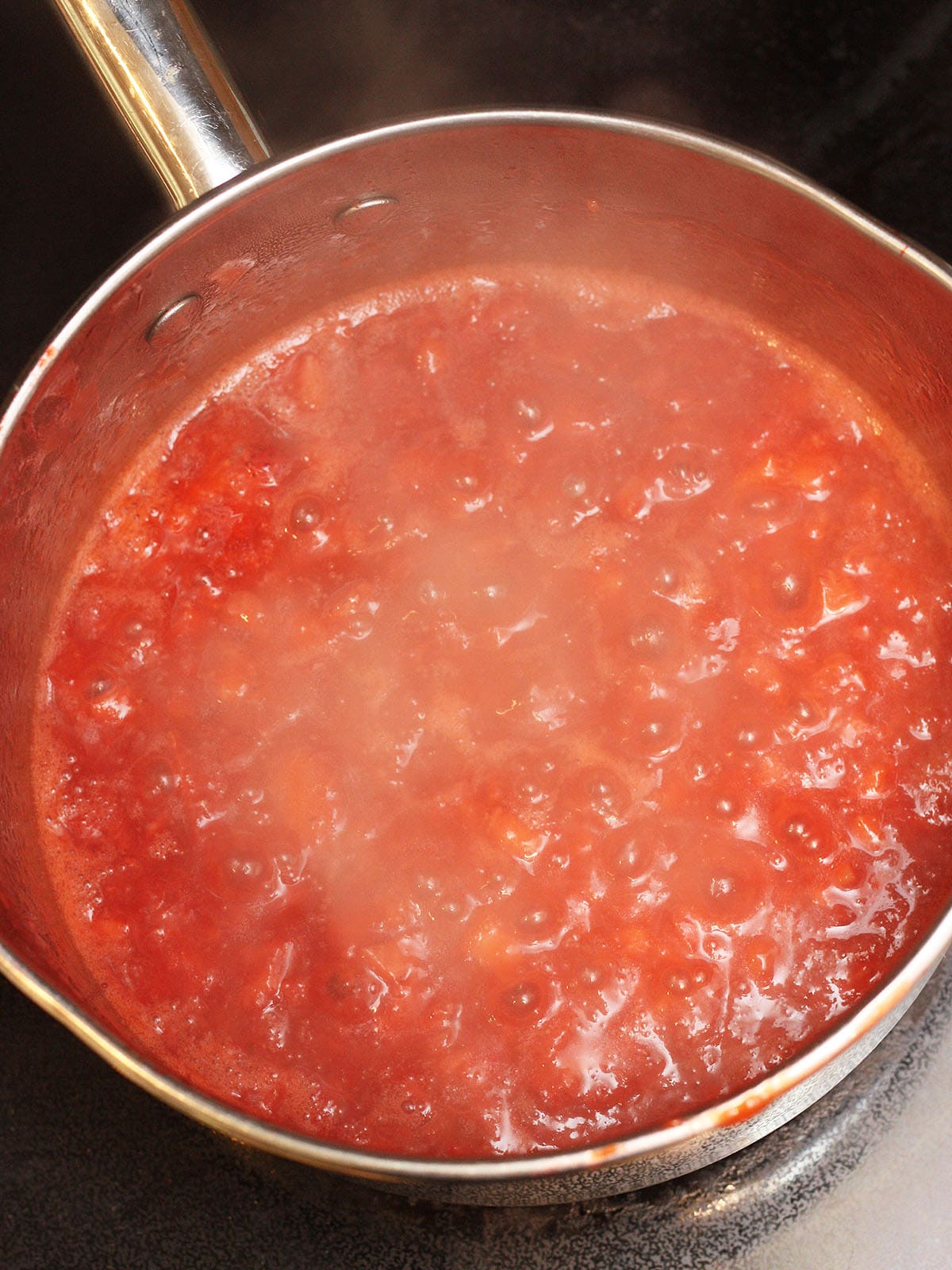 Homemade strawberry preserves at a full rolling boil in a metal saucepan.