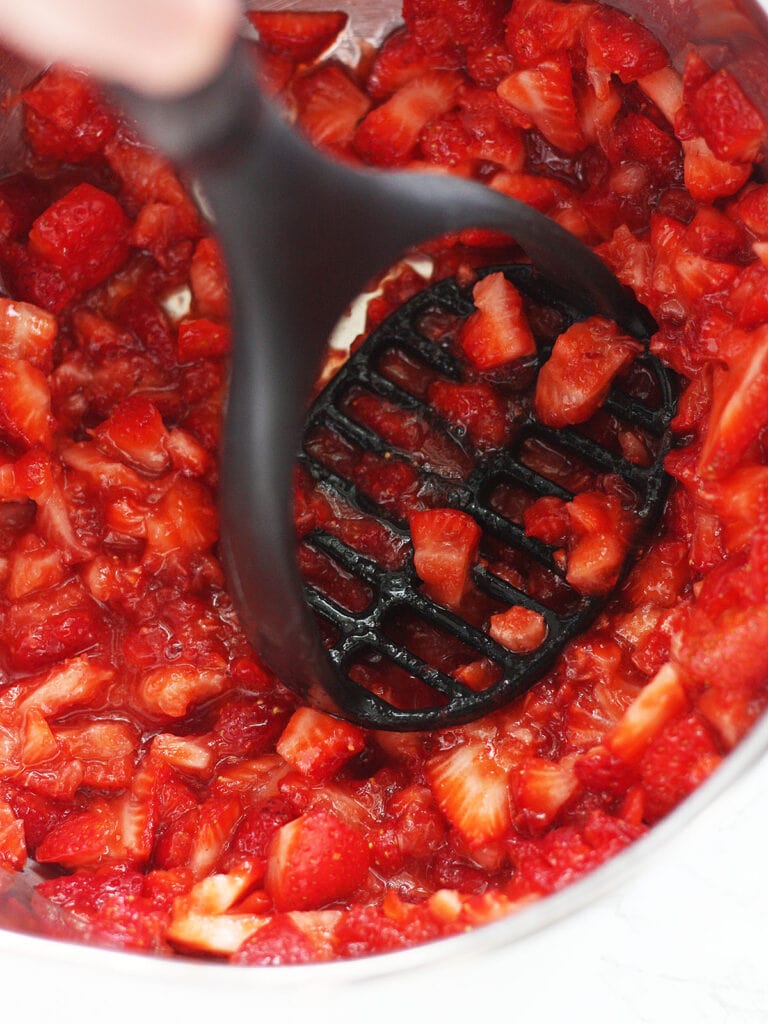 Mashing cut up strawberries with a potato masher.