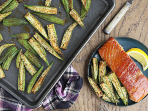 Roasted okra served alongside a salmon filet on a blue plate.