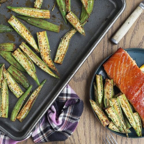 Roasted okra served alongside a salmon filet on a blue plate.