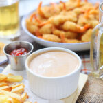 White condiment bowl of Mississippi comeback sauce with French fries and a platter of fried shrimp in the background.