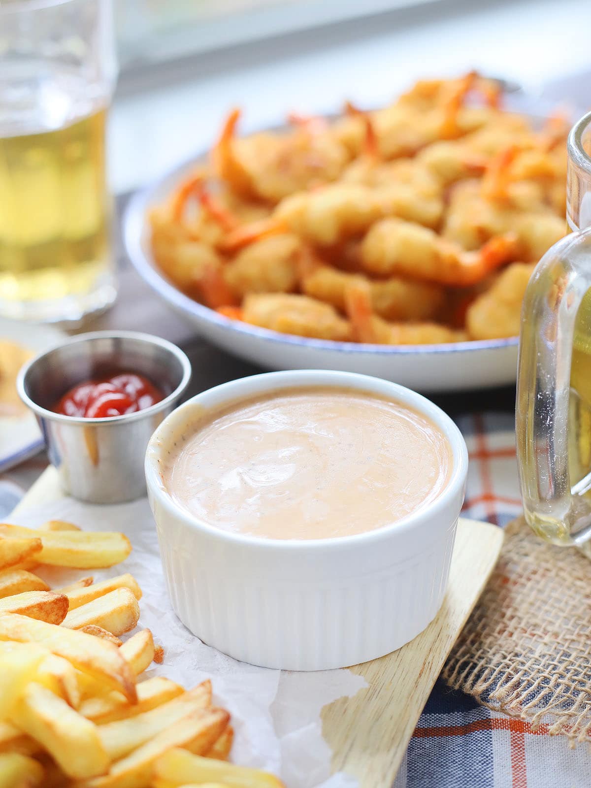 White condiment bowl of Mississippi comeback sauce with French fries and a platter of fried shrimp in the background.