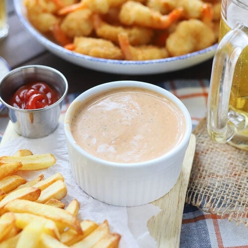 White condiment bowl of Mississippi comeback sauce with French fries and a platter of fried shrimp in the background.