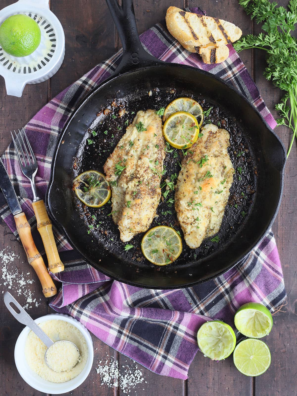 Two catfish fillets garnished with slices of lime in a cast iron skillet.