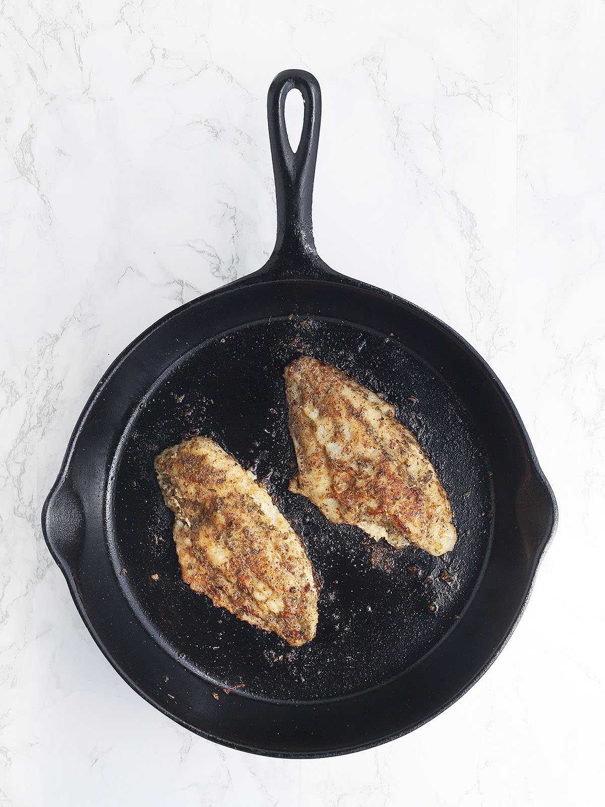 Two catfish fillets in a cast iron skillet after they have been seared on both sides.