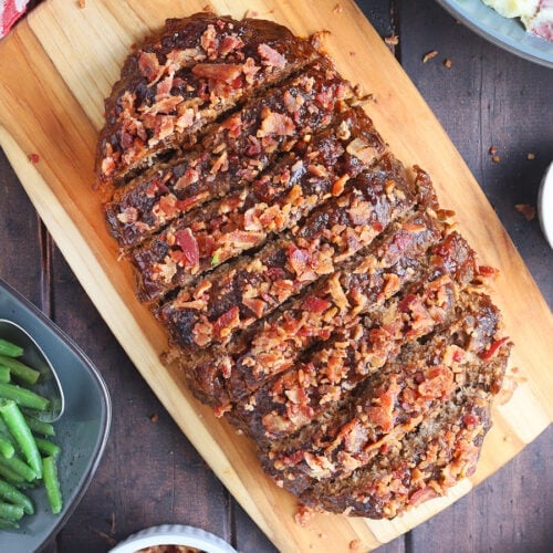 Sliced BBQ meatloaf on a wooden cutting board.