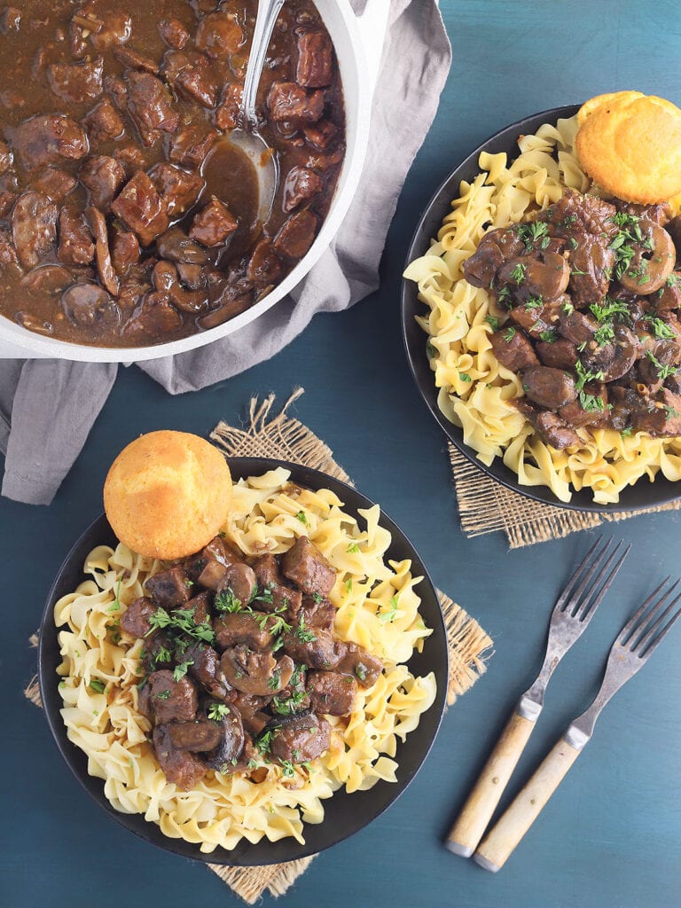 Two bowls of braised beef tips over egg noodles.