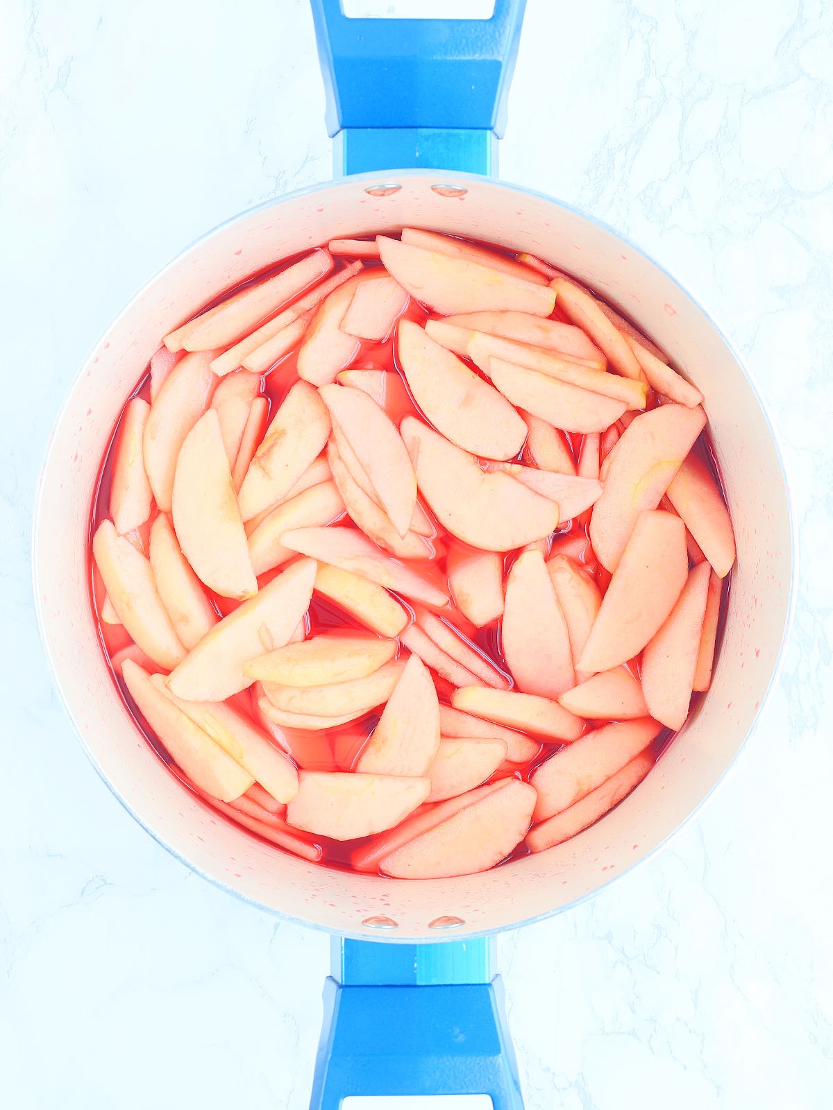 Sliced apples in a stock pot after being added to the Red Hots candy syrup.