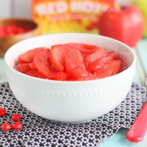 Two bowls of Red Hot cinnamon apples with with fresh apples and a dish of cinnamon imperiay candy on the side.