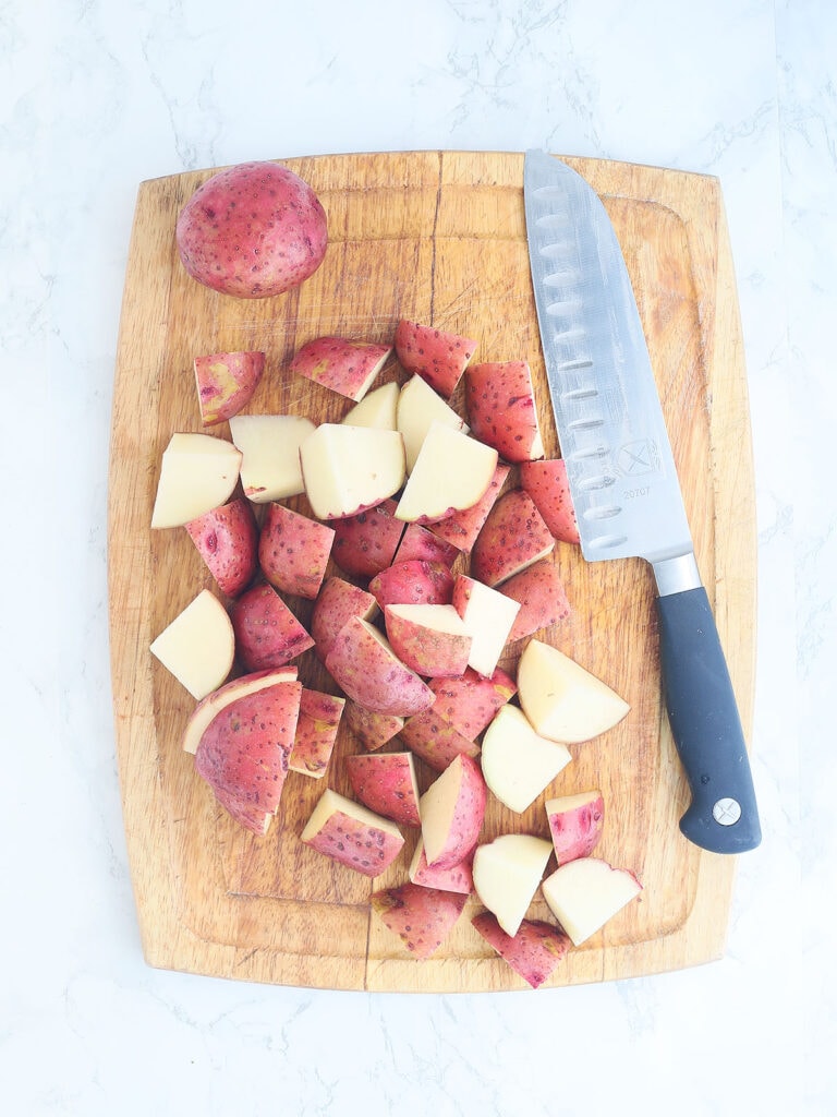 Quartered potatoes with a knife on a wood cutting board.