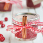 A jar of Christmas Jam garnished with red ribbon and a cinnamon stick.