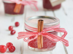A jar of Christmas Jam garnished with red ribbon and a cinnamon stick.