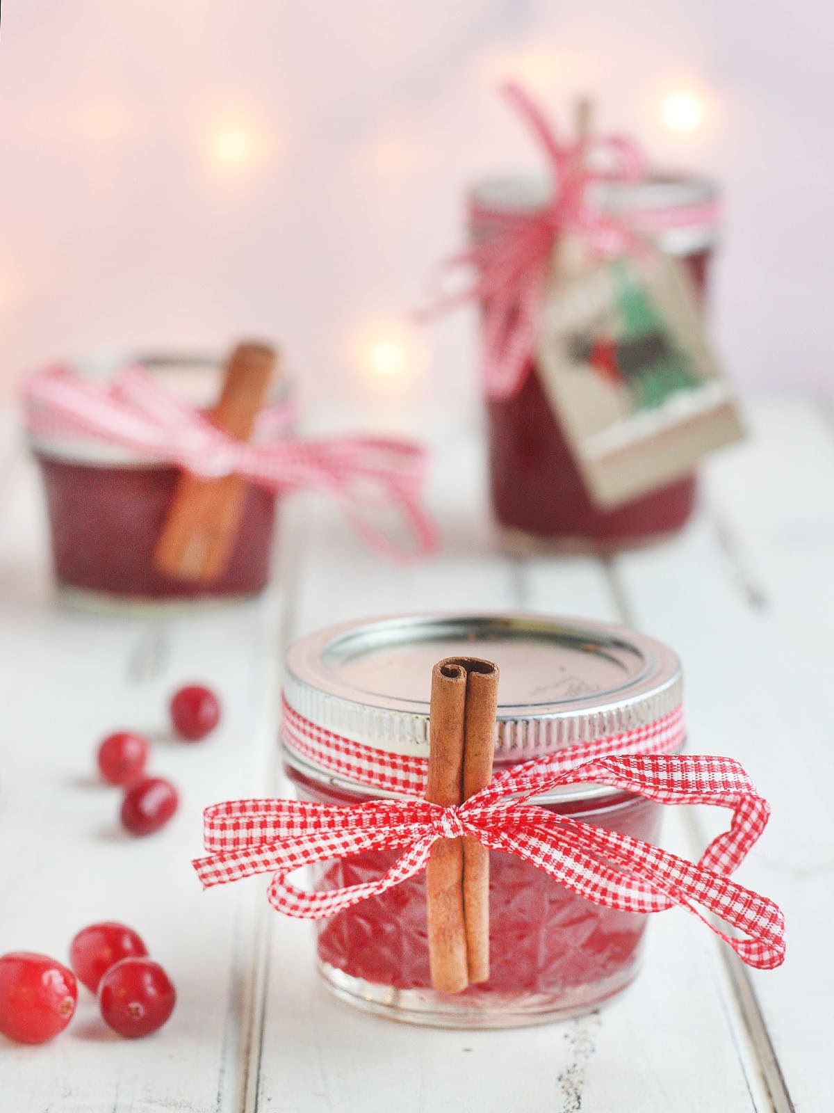 Jars of Christmas Jam garnished with red ribbon and cinnamon sticks.