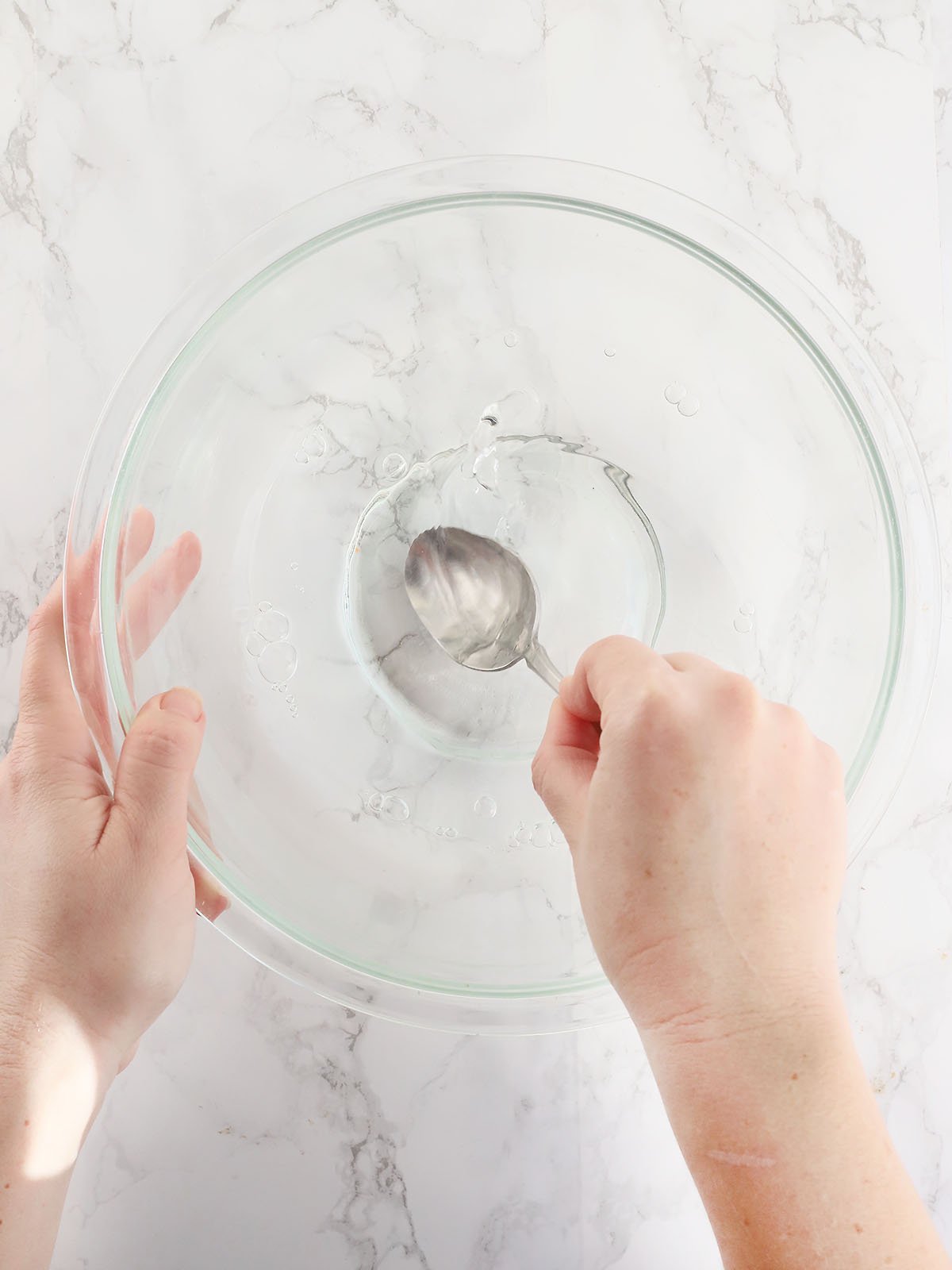 Hand dissolving the baking soda in a mixing bowl of water.
