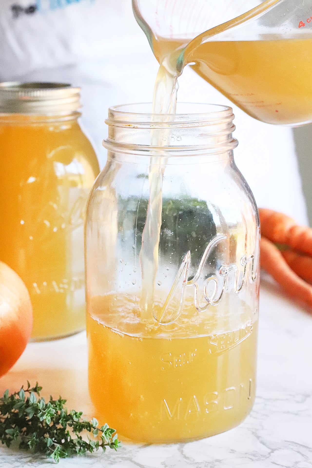 Pouring homemade chicken stock into a glass jar.