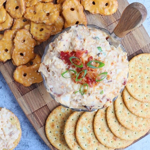 Dish of spicy pimento cheese topped with chopped bacon and green onions surrounded by pretzels and crackers.