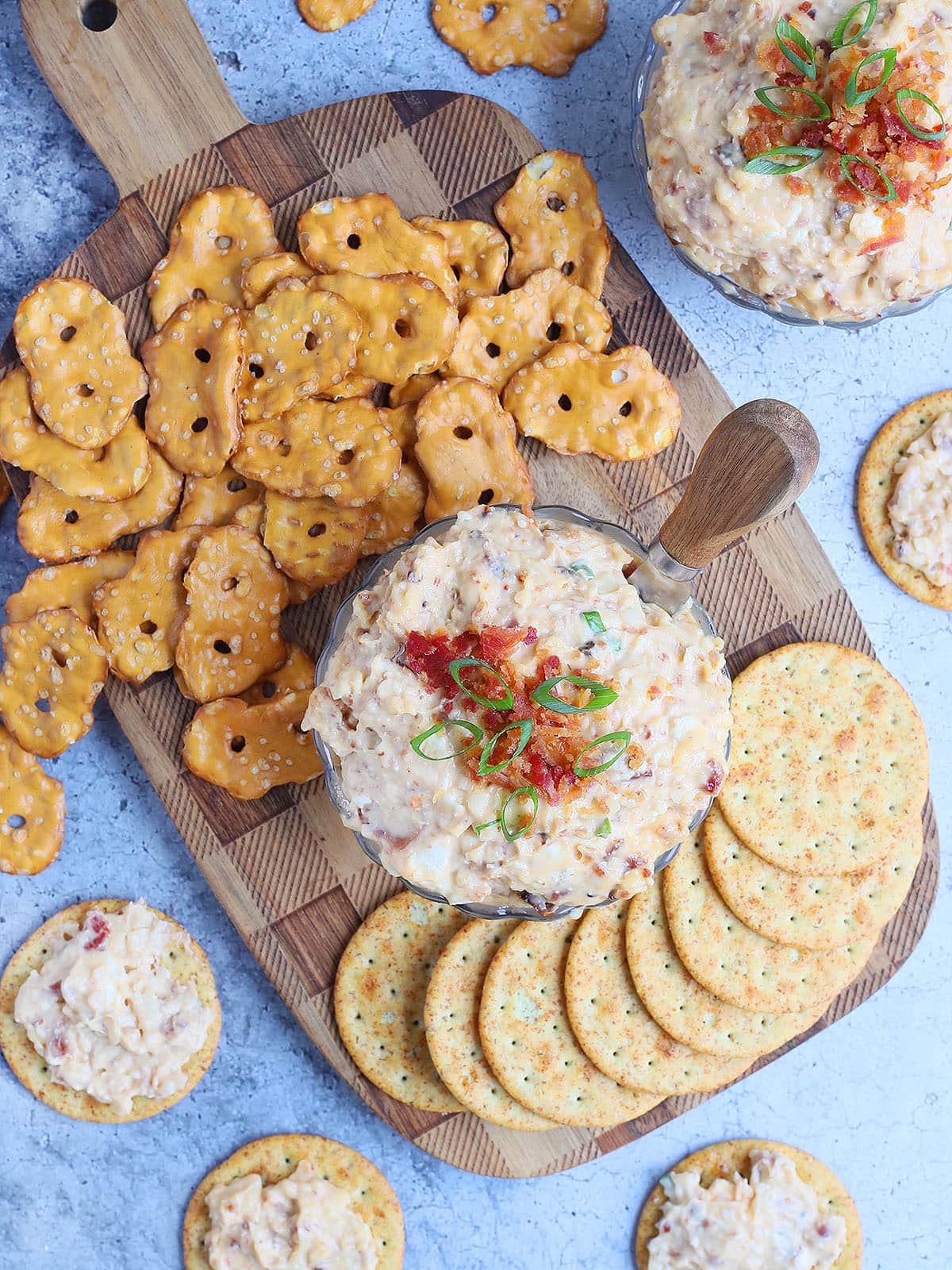 Dish of spicy pimento cheese topped with chopped bacon and green onions surrounded by pretzels and crackers.