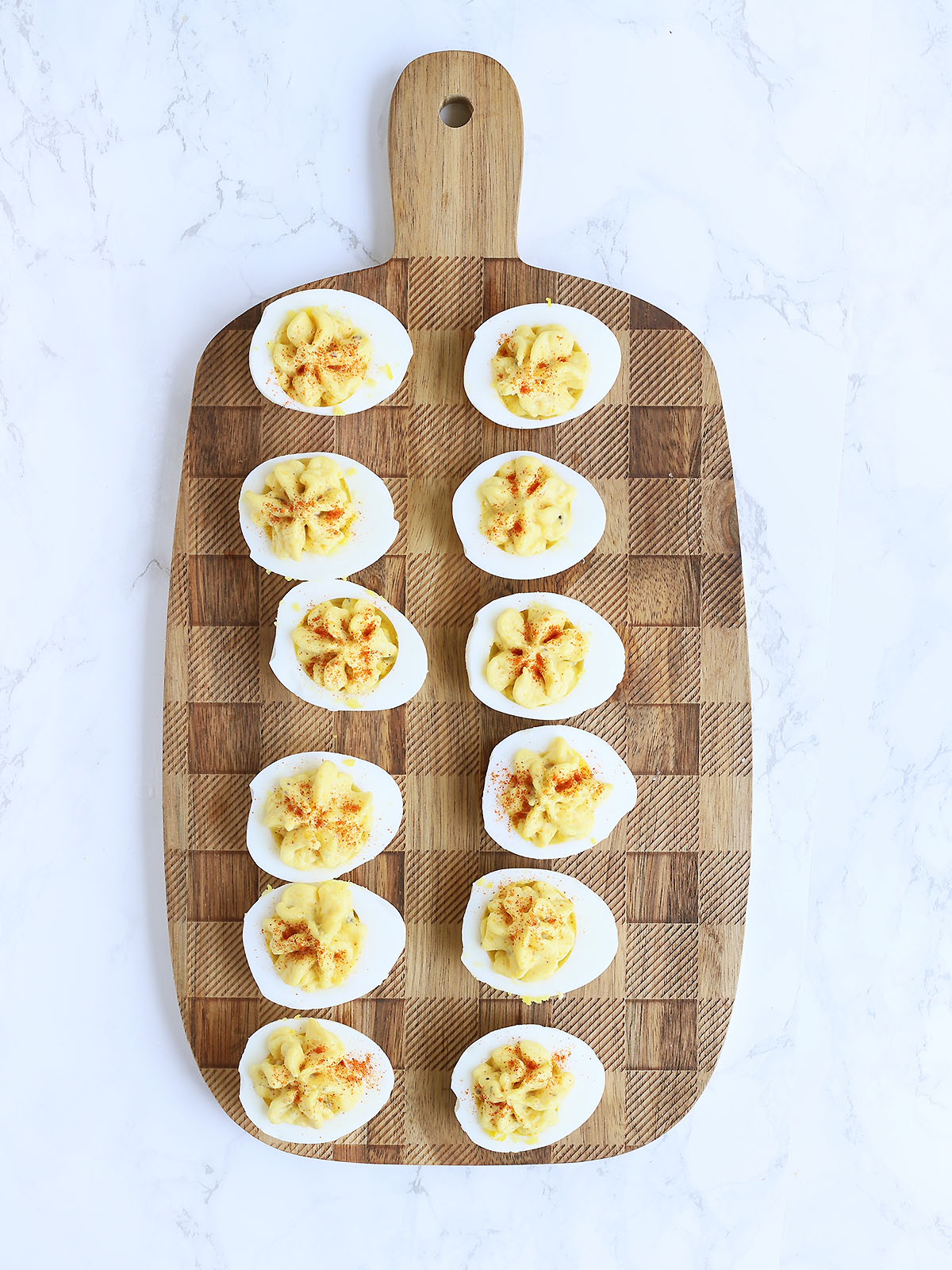 Six deviled eggs garnished with paprika on a serving board.